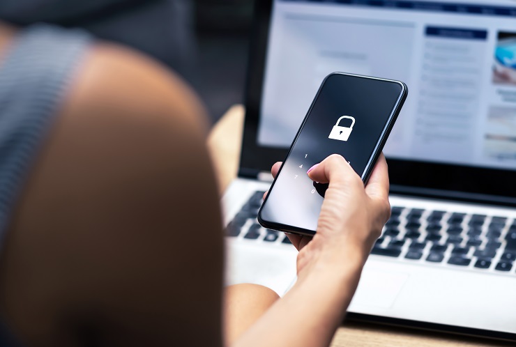 Kobieta trzymająca smartfon, na ekranie jest kłódka, a w tle laptop.
