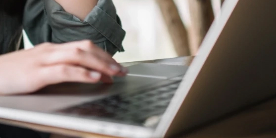 Osoba pracująca na laptopie, zbliżenie na dłonie na klawiaturze.