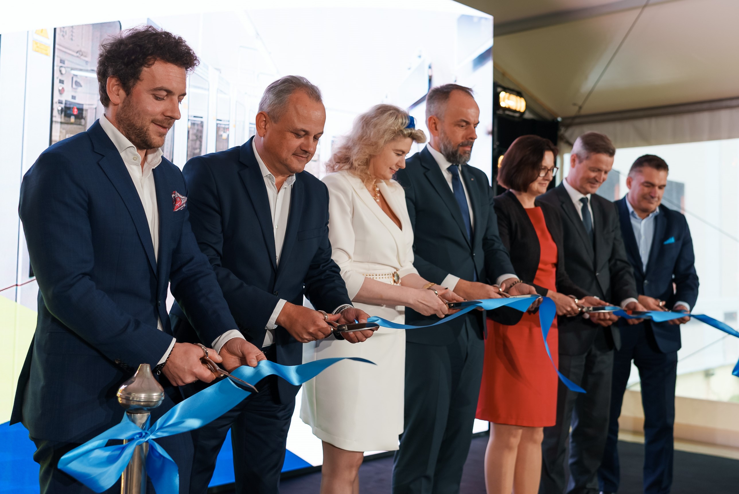 Grupa osób uroczyście przecina niebieską wstęgę podczas otwarcia.