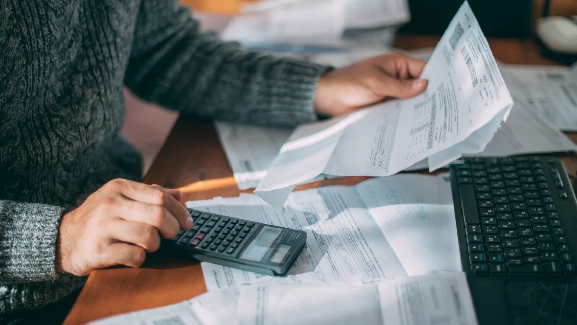 Zbliżenie na dłonie, dokumenty, kalkulator oraz laptop.