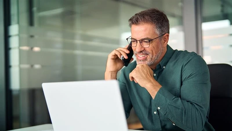 Mężczyzna rozmawia przez telefon i patrzy na ekran laptopa.